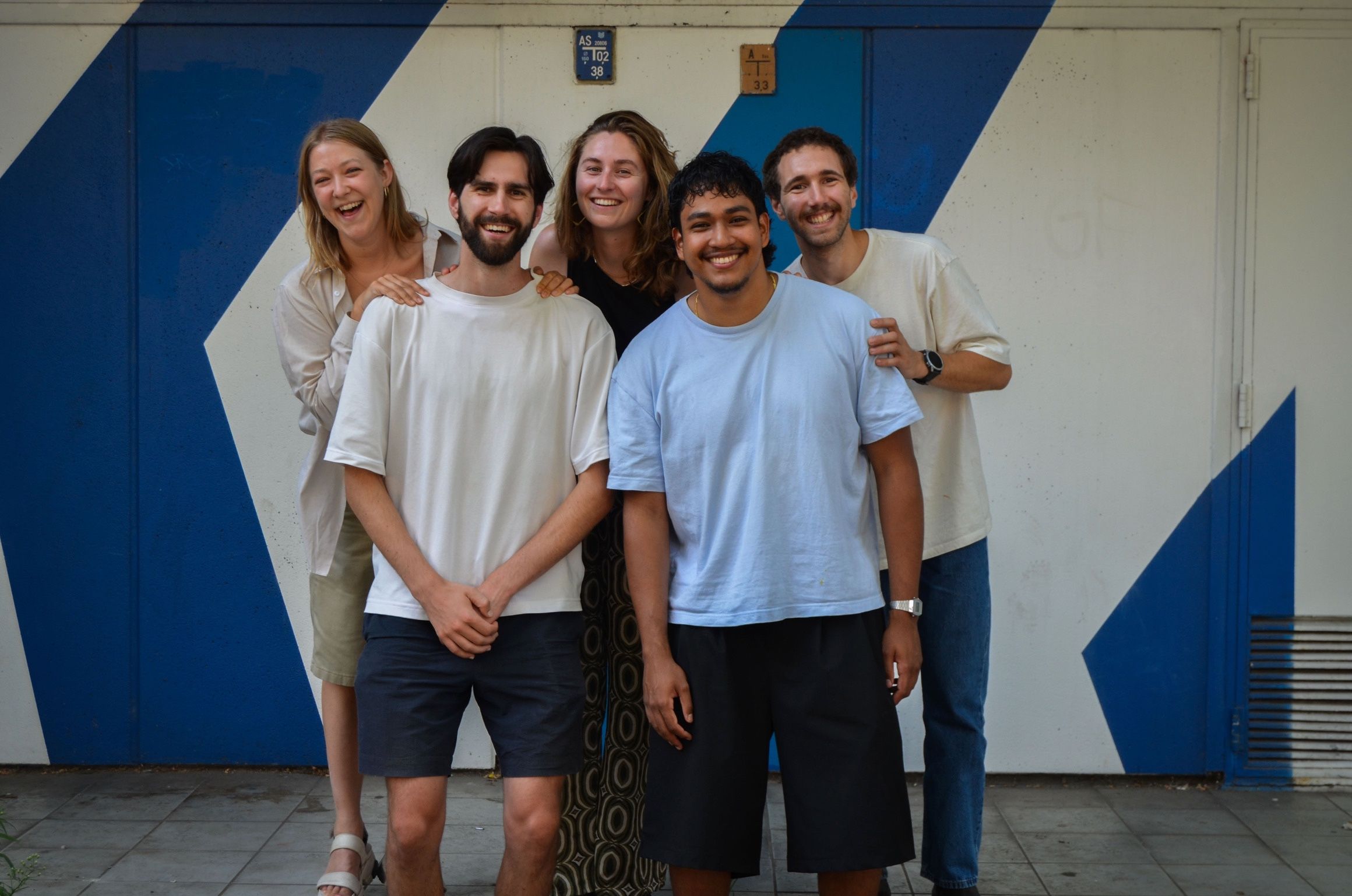 Five smiling Parai team members in front of a blue and white mural